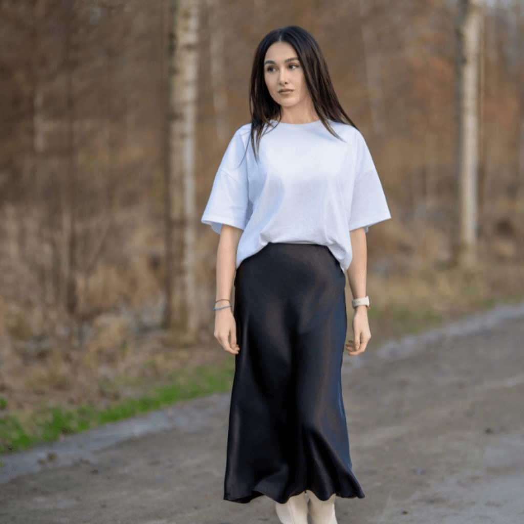 Woman wearing a white oversized t-shirt and a black mid-length pencil skirt, posing in a natural outdoor setting with a serene expression.