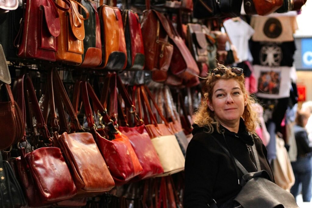 A woman standing in front of a store display filled with an assortment of handmade leather bags for women, showcasing a variety of styles and colors.