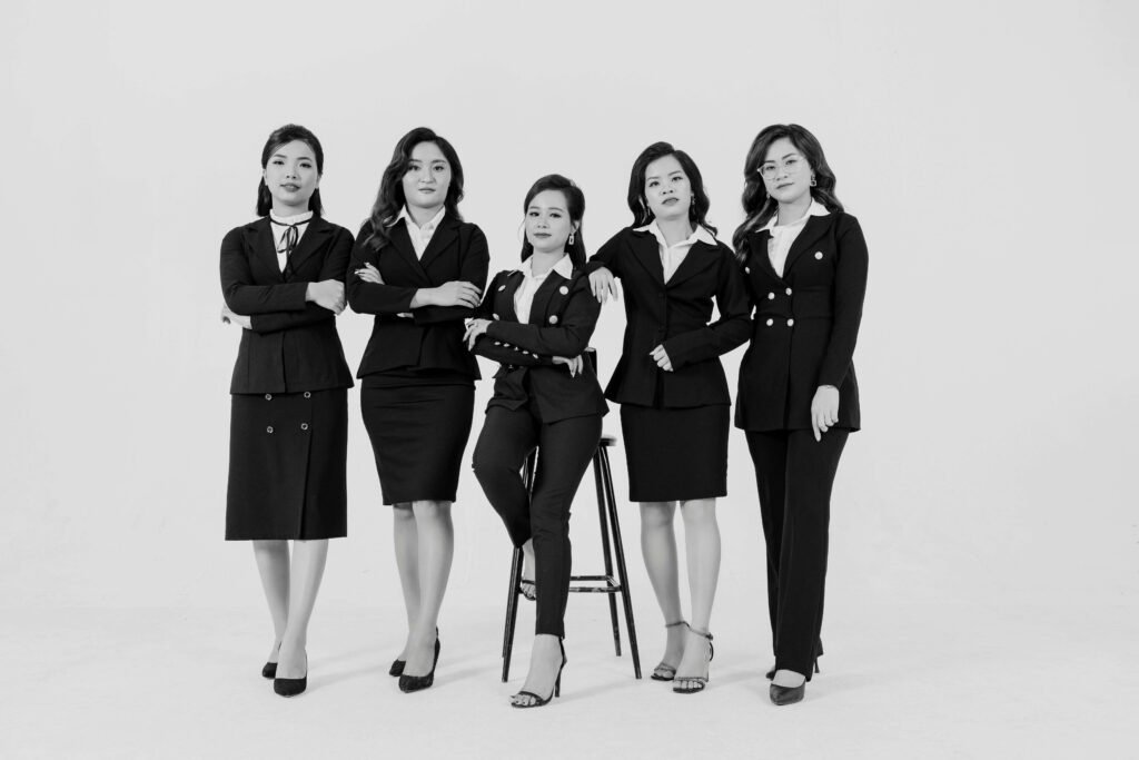 A group of women confidently posing in stylish professional office wear for women, including blazers, skirts, and trousers, exuding elegance and professionalism in a monochromatic setting.